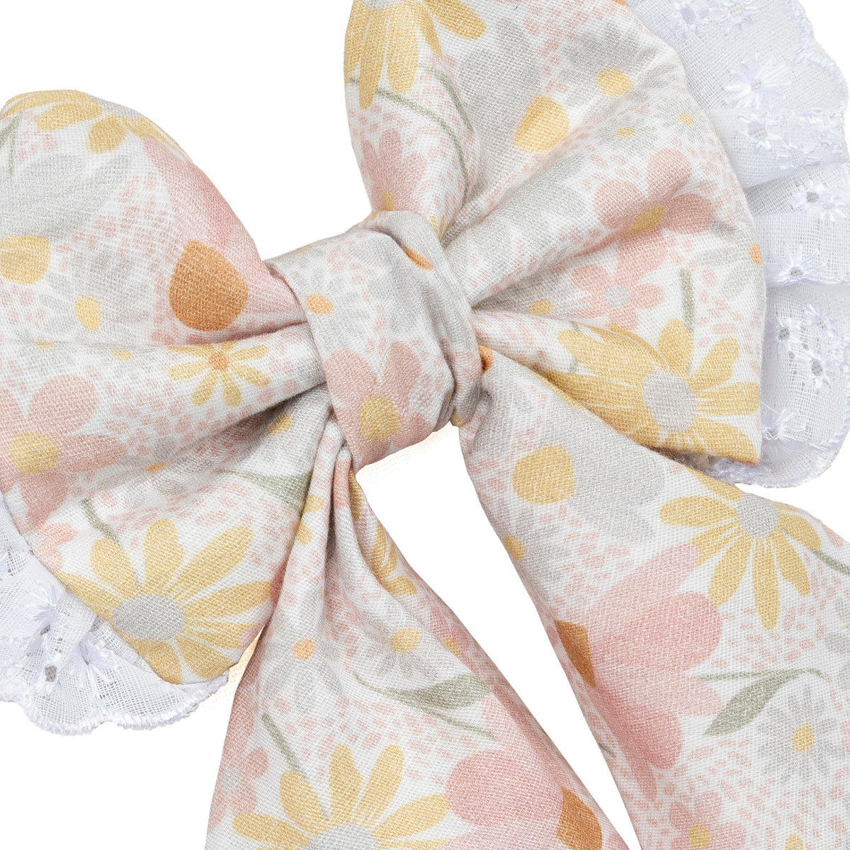 A close-up of a fabric dog bow with a pastel floral print on a white background, featuring yellow daisies, pink flowers, and green leaves, finished with white lace trim.